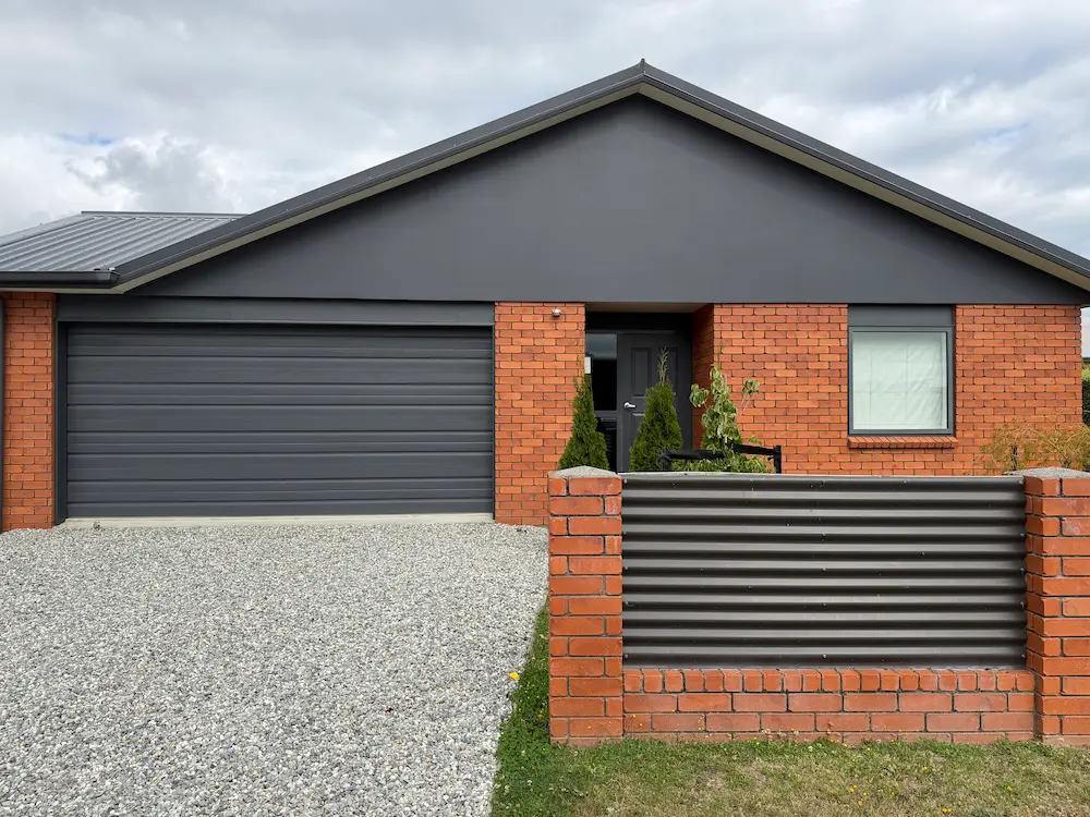 Finished exterior painting works on gable end of a Wānaka home — fresh dark grey paint and brick